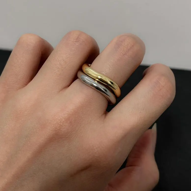 Hand wearing a gold and silver ring on a neutral background