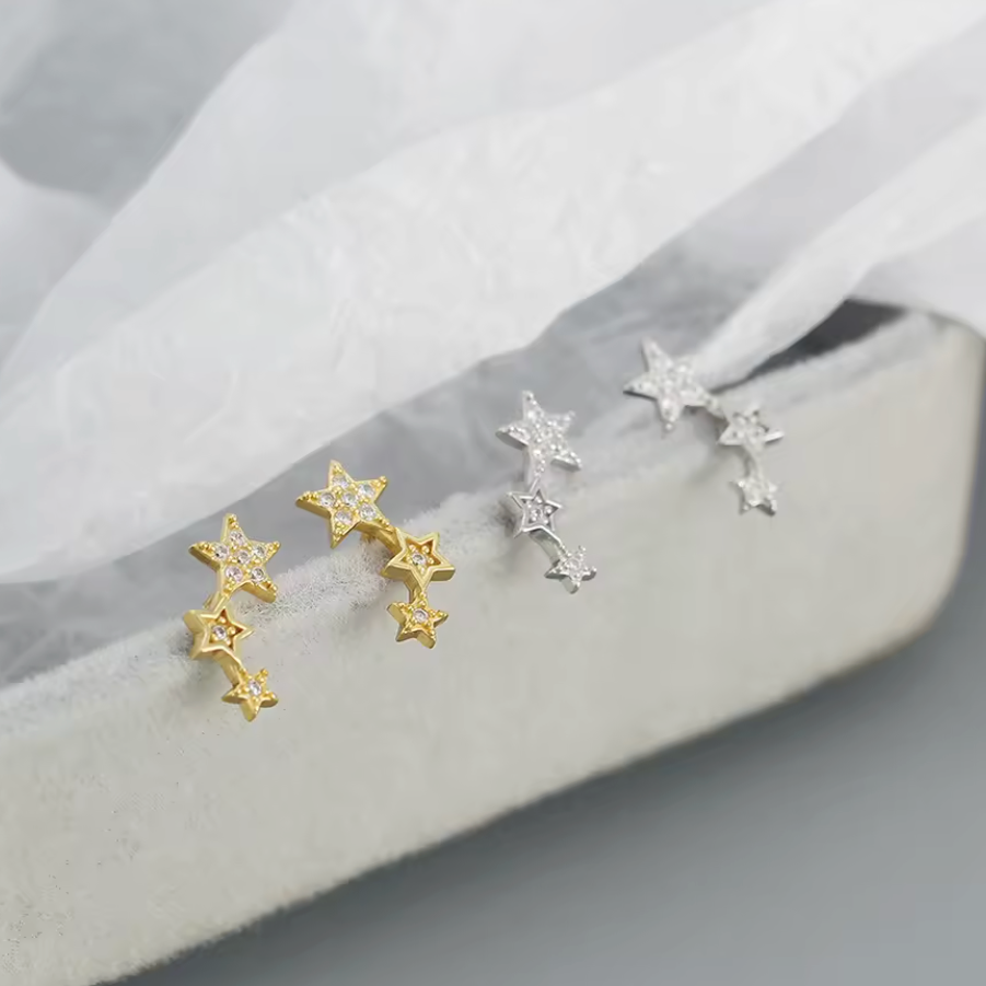 Star-shaped earrings in gold and silver on a soft fabric background