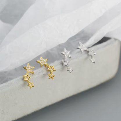 Star-shaped earrings in gold and silver on a soft fabric background