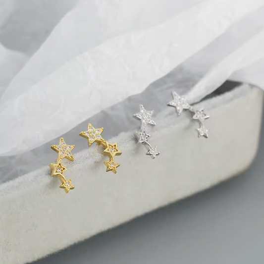 Star-shaped earrings in gold and silver on a soft fabric background