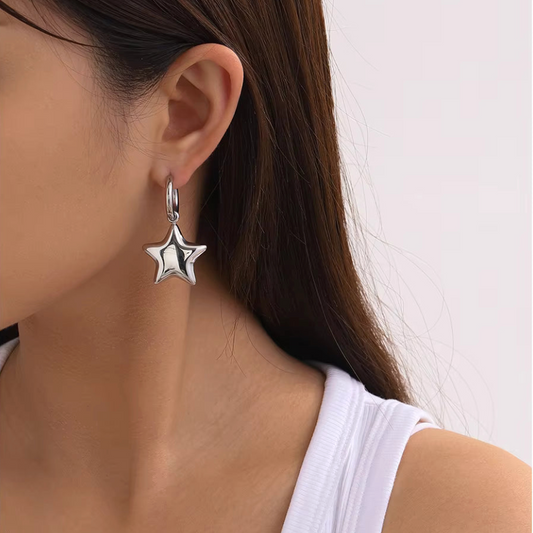 Star-shaped silver earring worn by a person with a plain background